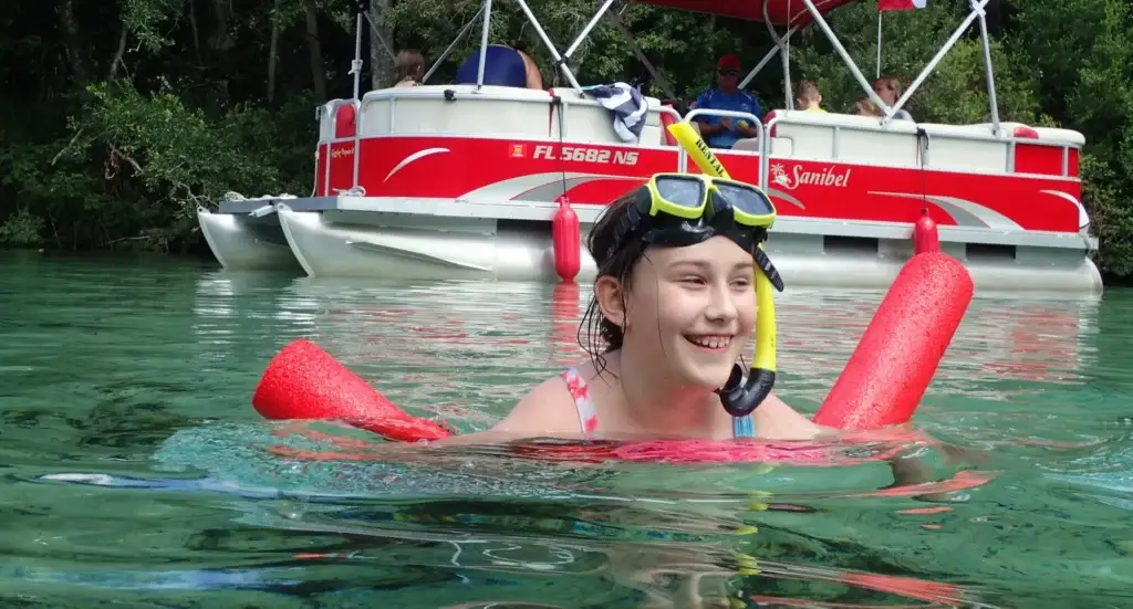 A smiling snorkeler in the water with the pontoon boat behind her