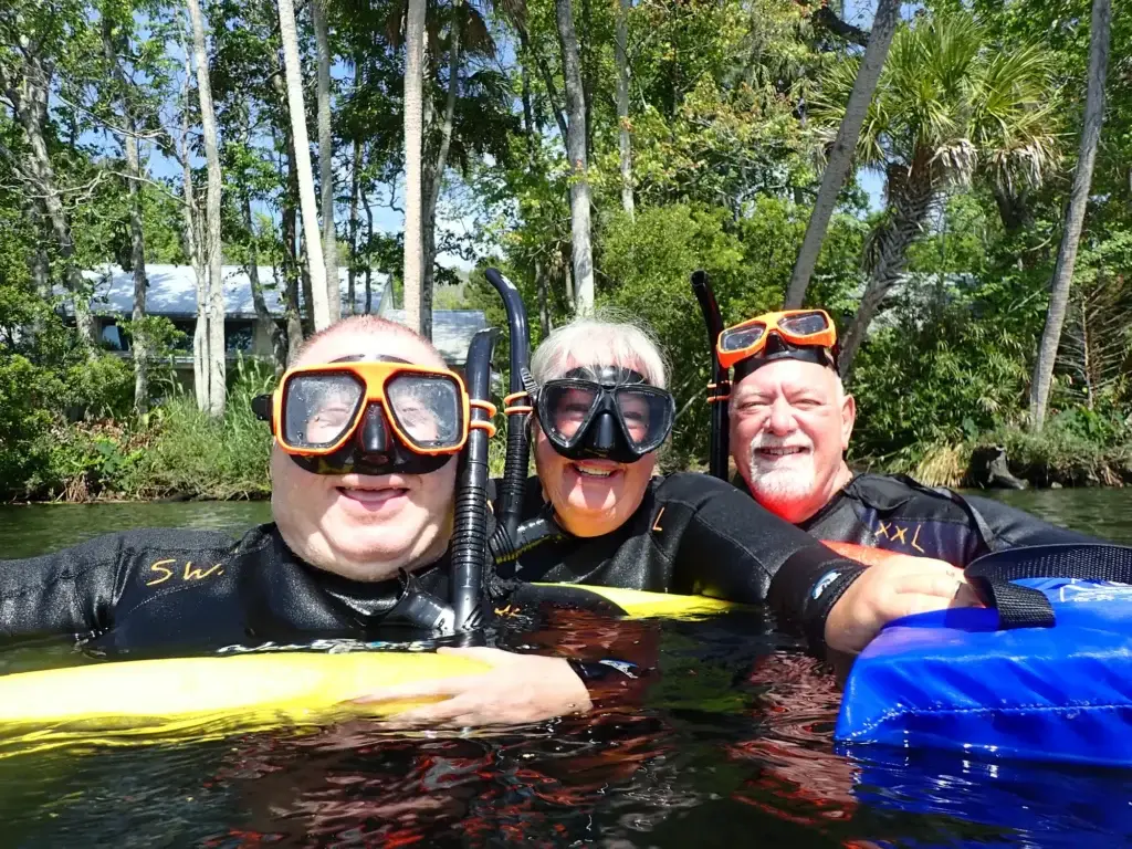Three guests in snorkel masks grinning in the river