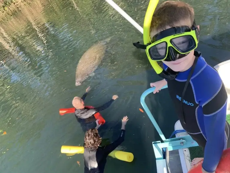 Kids in wetsuits and snorkels at the boat ladder with a manatee below